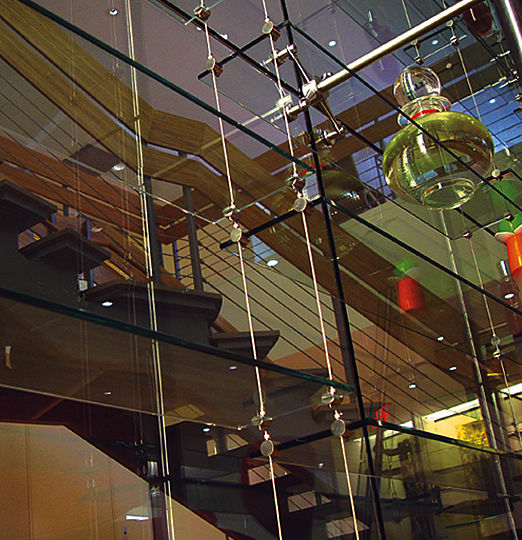 Two-story high structure of suspended glass shelves screens the view from the open space into the conference rooms of both levels.  The entire glass structure is subtly lit by an arrangement of deeply recessed fluorescent lights concealed along its vertical edge.